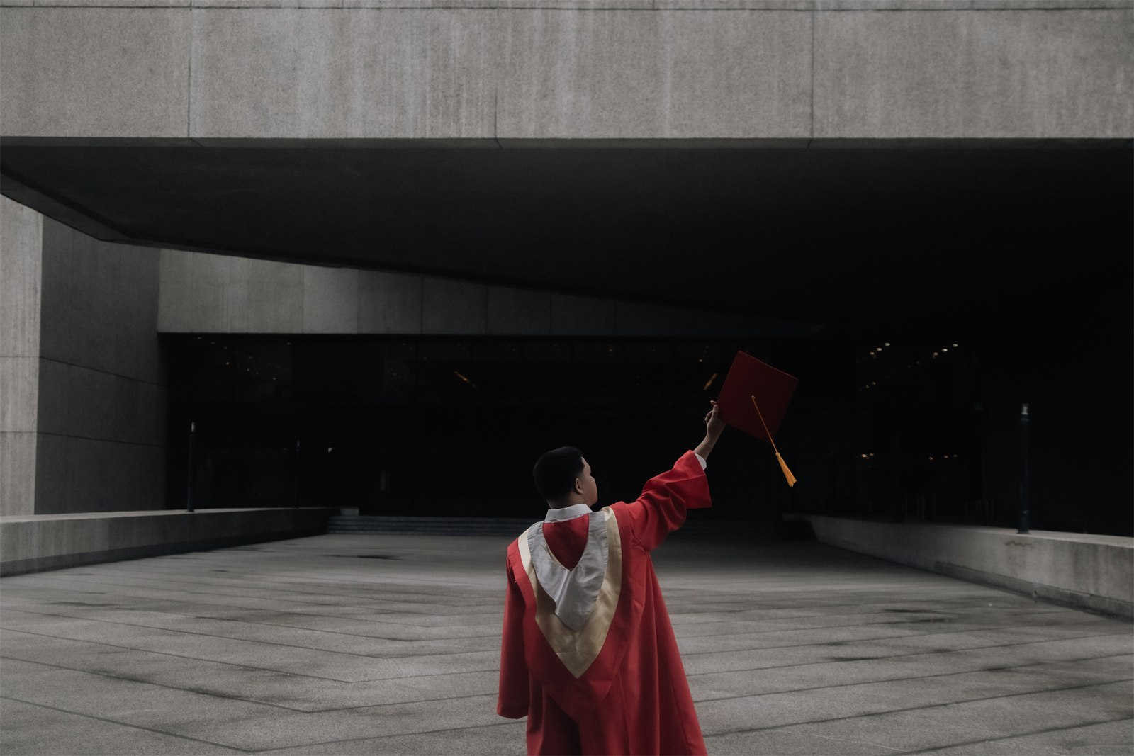 Ronan in his graduation gown, holding his cap up outside a building.